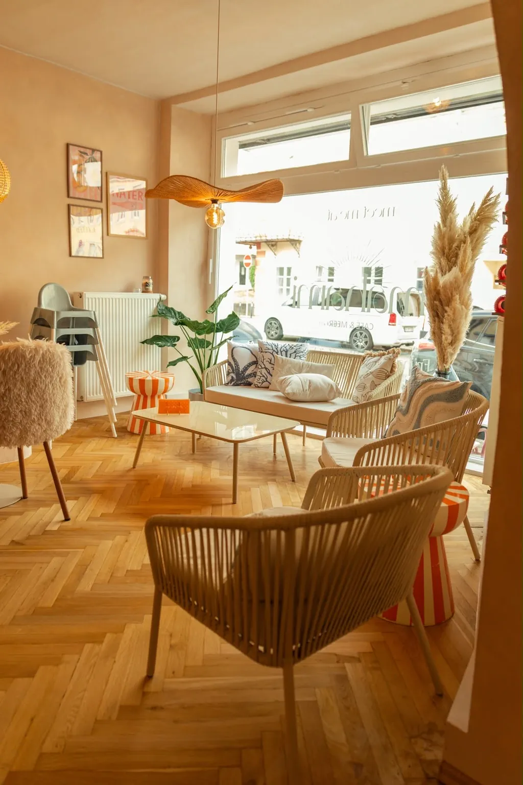 Heller Gastraum mit Rattan-Sesseln, Pflanzen und Pampasgras vor dem großen Fenster.
