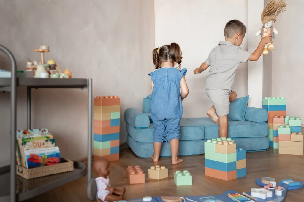 Zwei Kinder spielen in der Spielecke zwischen großen, bunten Bausteinen, vor einem blauen Sofa.